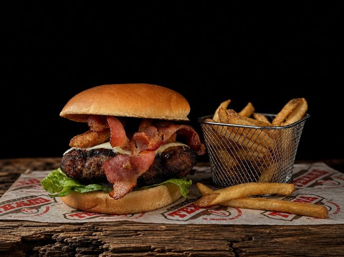 Hamburguesa con tocino y canasta de papas sobre papel con el logotipo de La Cabaña Texana